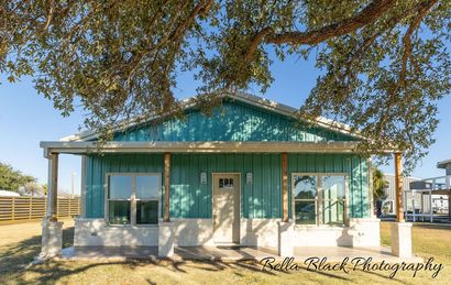 Turquoise cottage with a porch under a large tree in a sunny rural setting