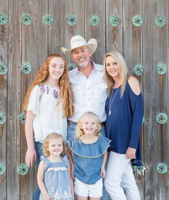 Family of five posing in front of a rustic wooden wall with teal decorative accents