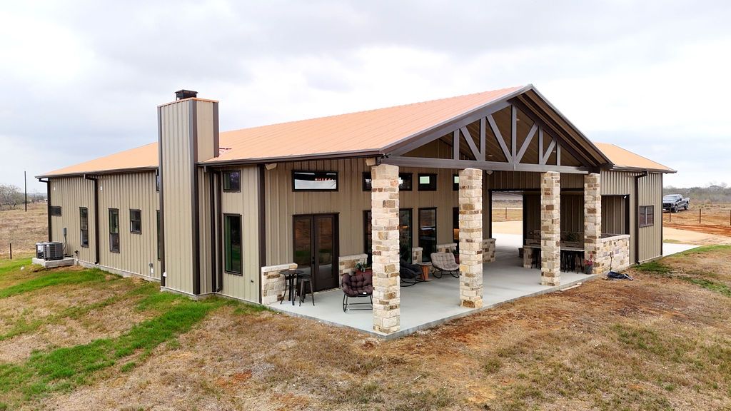 Modern stone pavilion with a covered patio and exposed wooden beams on a grassy lot