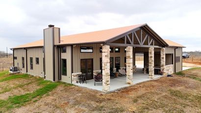 Modern stone pavilion with a covered patio and exposed wooden beams on a grassy lot