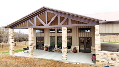 Small stone-front porch with wooden gabled roof, potted plants, and glass doors on a modern building