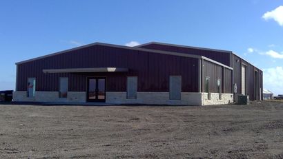 Large dark industrial building with a metal roof on a flat gravel lot under a blue sky