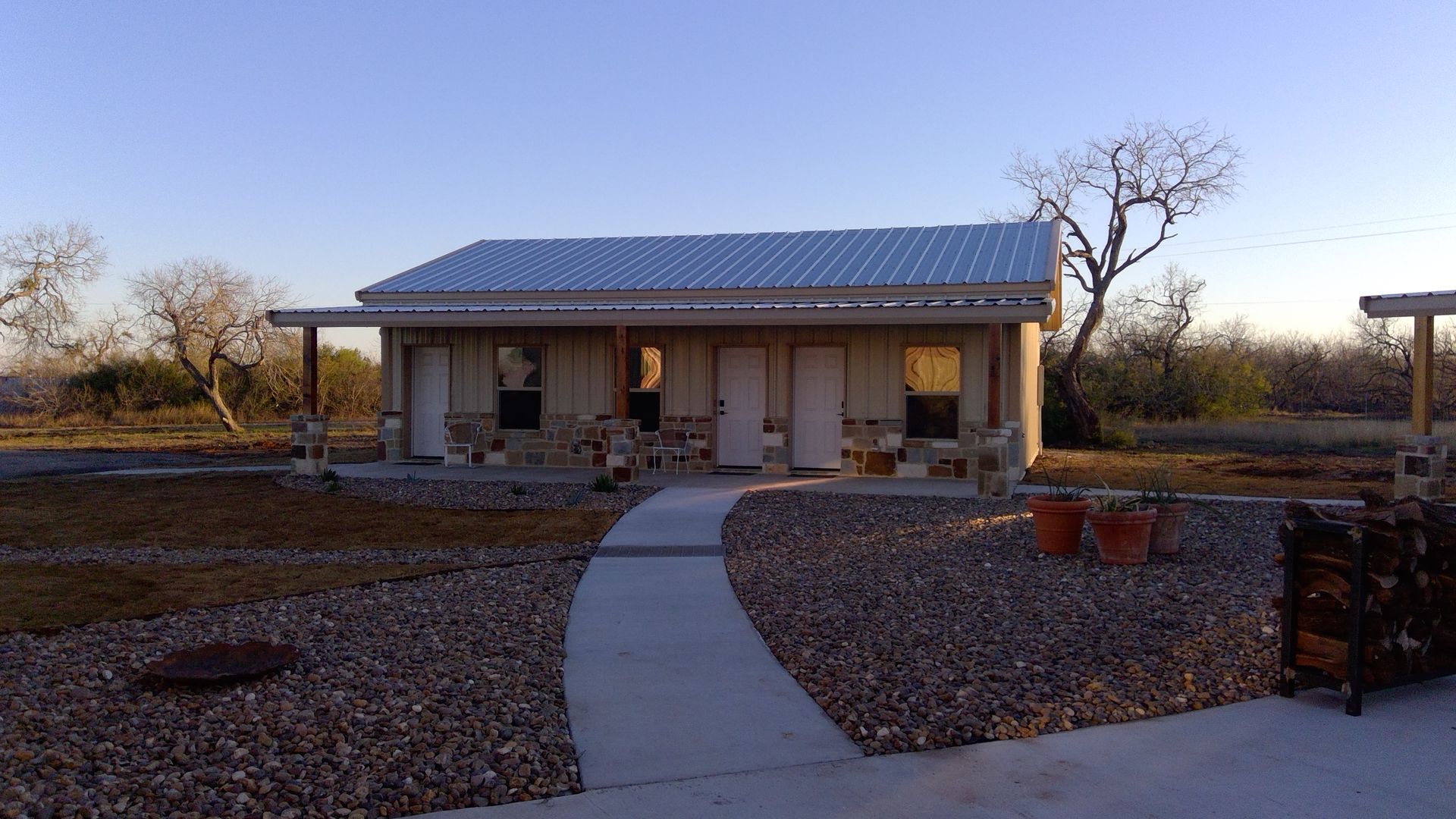 Small house with a blue roof and front porch, seen at dusk along a curved concrete path.
