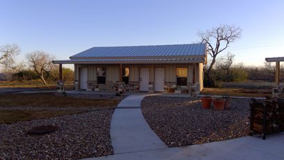 Small house with a blue roof and front porch, seen at dusk along a curved concrete path.