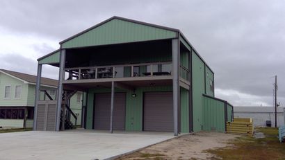 Green metal warehouse with a covered porch, roll-up doors, and a concrete driveway under cloudy skies