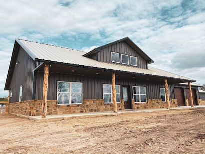 Rustic stone-and-wood house with a metal roof under a cloudy sky, fronted by bare dirt.