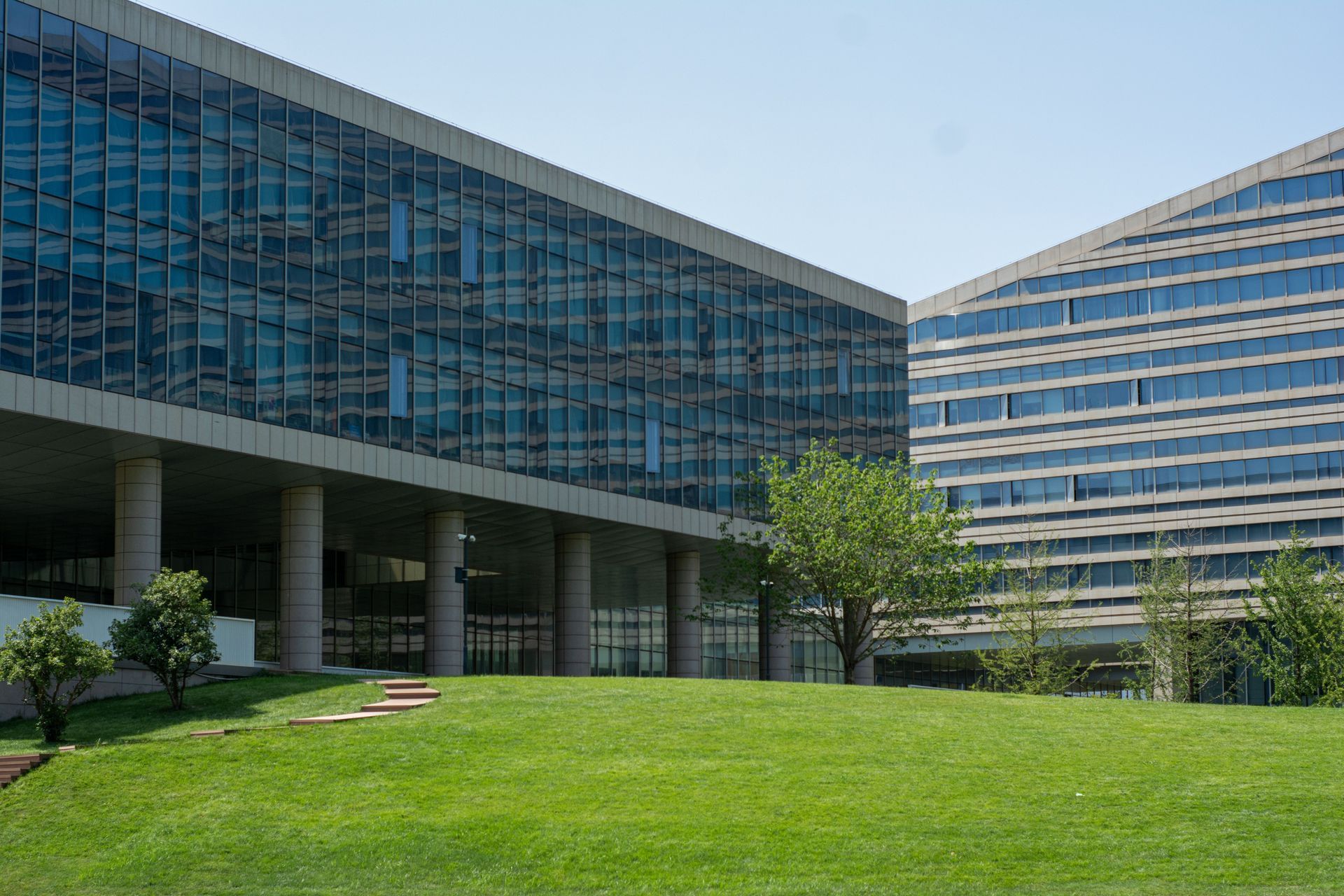 Modern glass office buildings beside a green lawn and trees under a clear sky