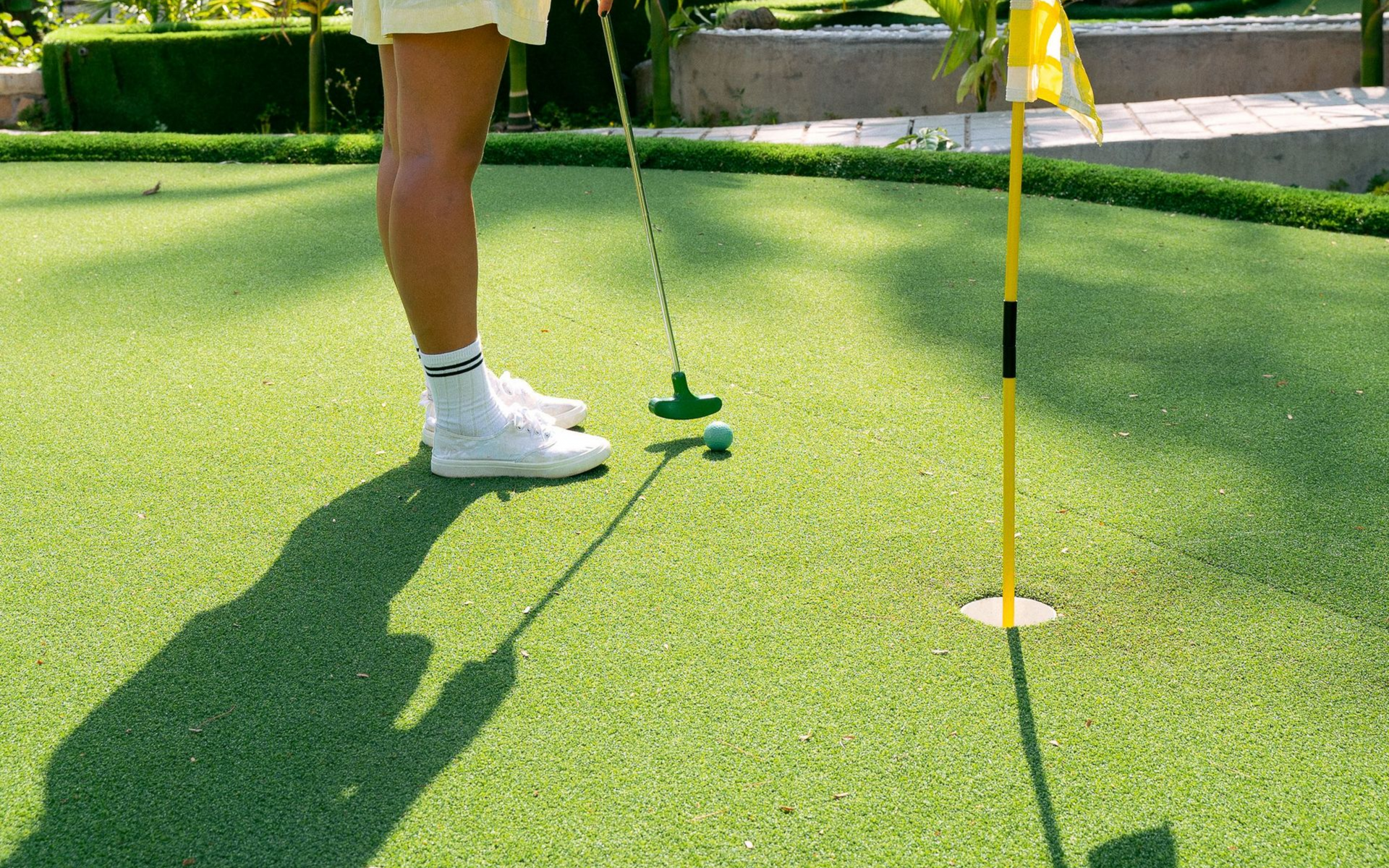 Golfer putting on a green with a flag and hole nearby, ball on the turf.