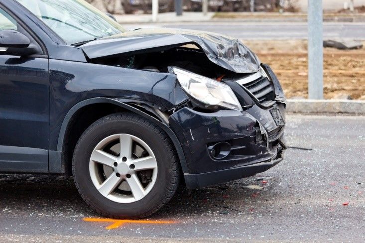 Damaged dark blue SUV after a collision with a crumpled hood and broken headlight on a road.