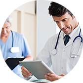 Doctor in white coat looking at a tablet; nurse in blue scrubs holding clipboard.