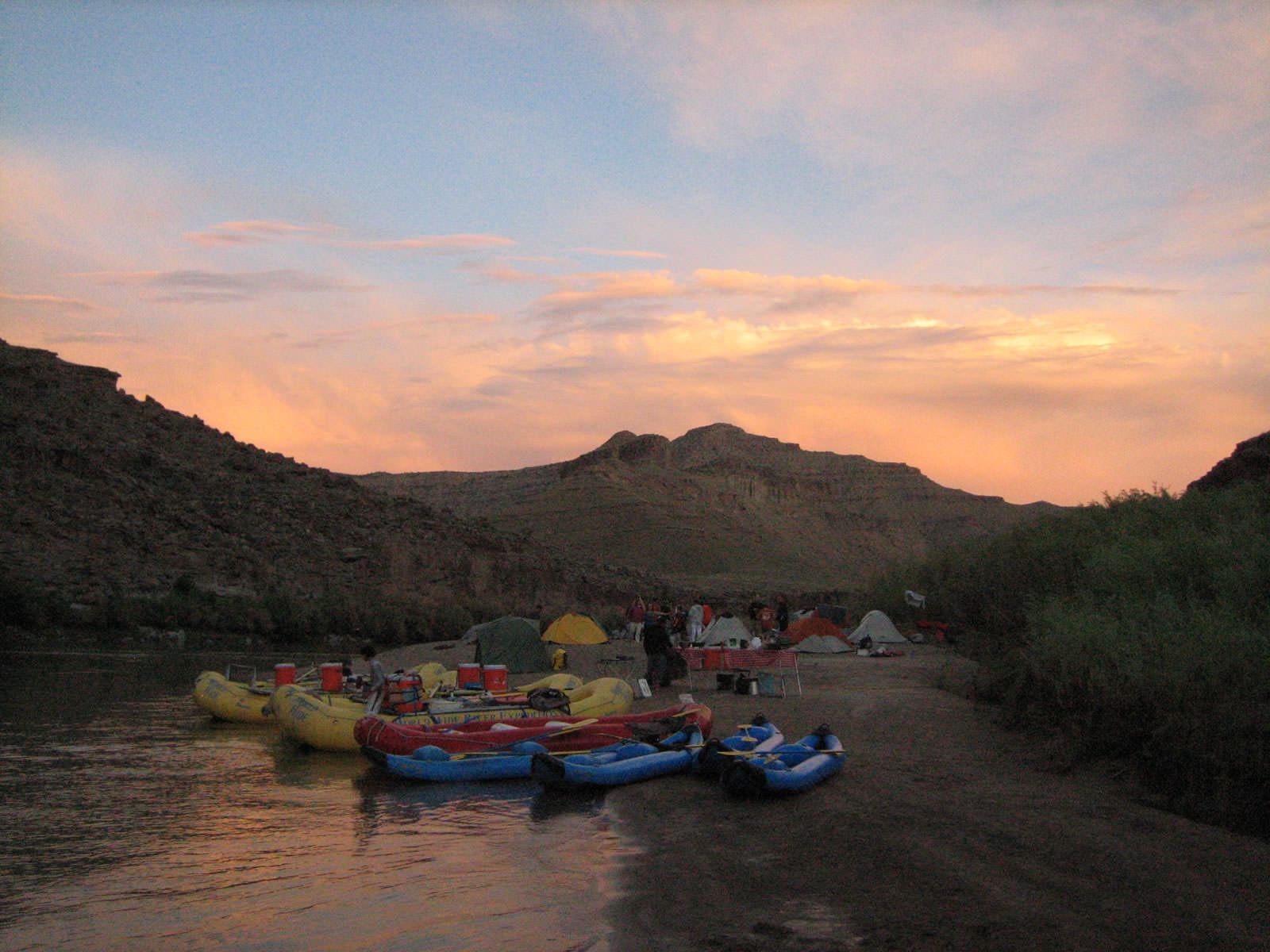 Rafts are lined up on the shore of a river at sunset