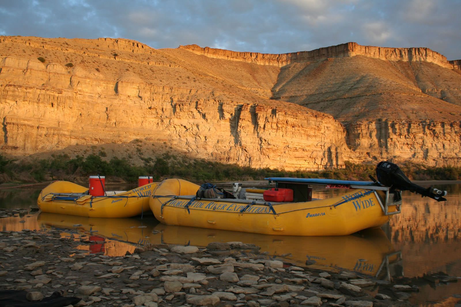 Two yellow rafts are docked in a river with mountains in the background