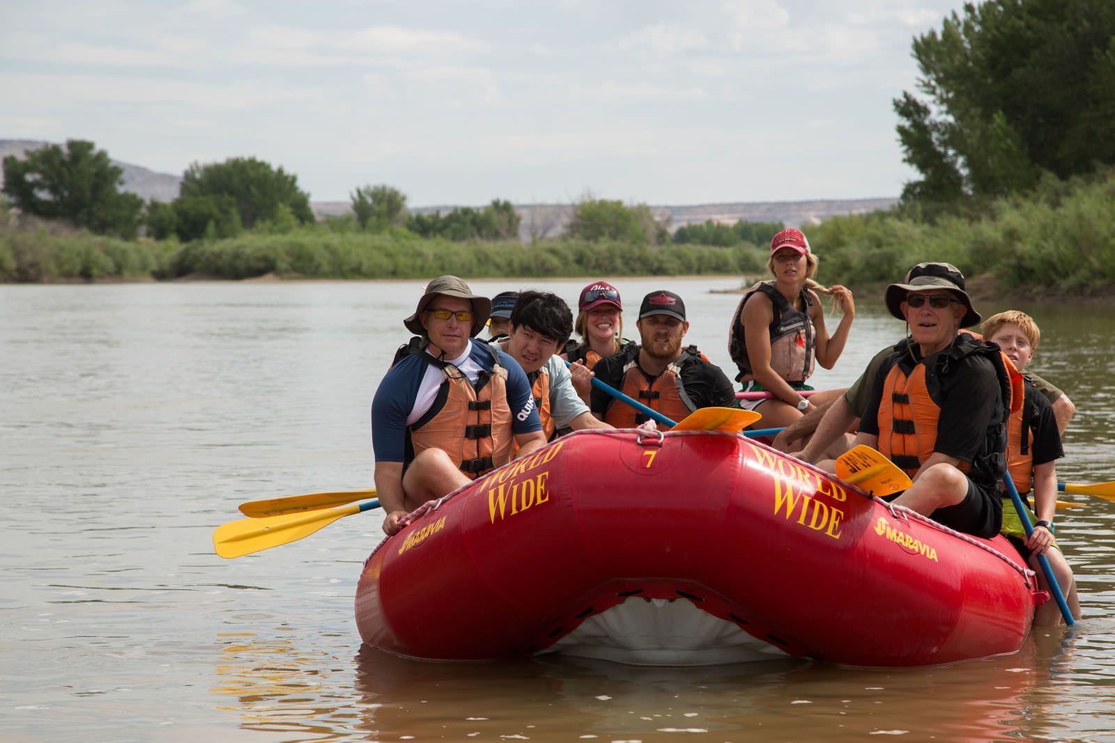 A group of people are rowing a red raft down a river.