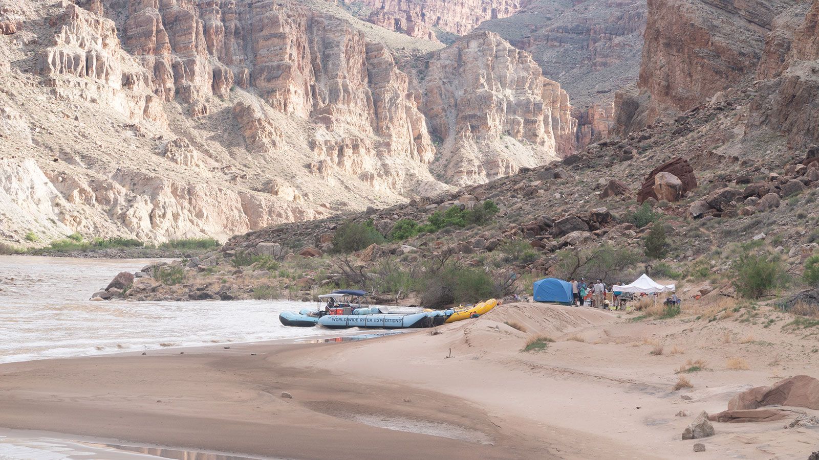 A group of rafts are sitting on a sandy beach next to a river.