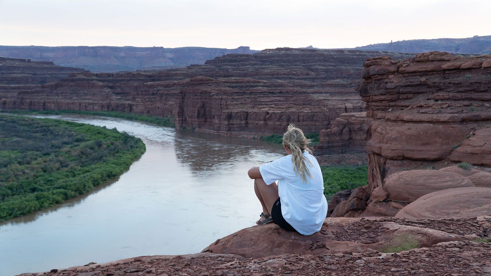 A woman is sitting on a rock overlooking a river.