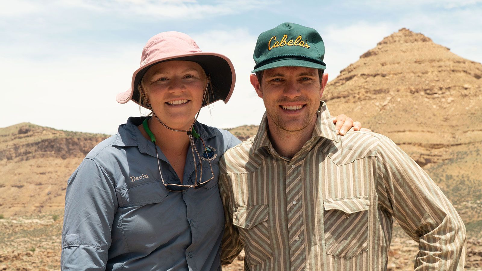 A man and a woman are posing for a picture in front of a mountain.