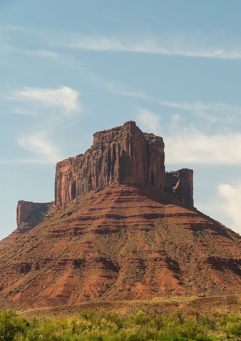 A large rocky mountain in the desert with a blue sky in the background.