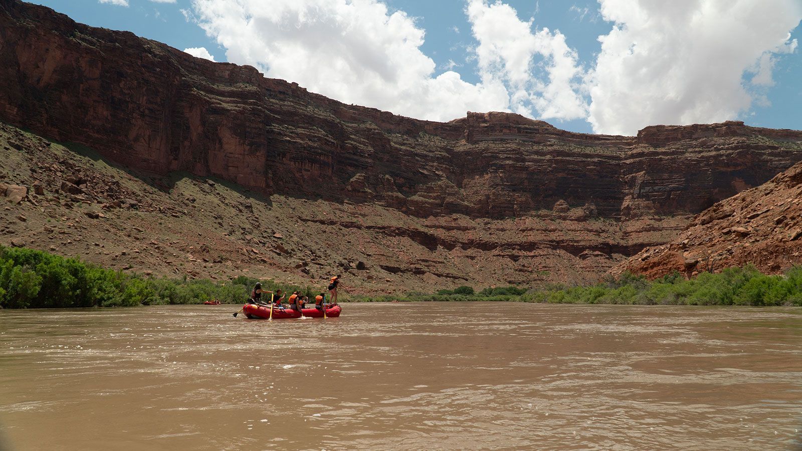 A group of people are rafting down a river with mountains in the background.