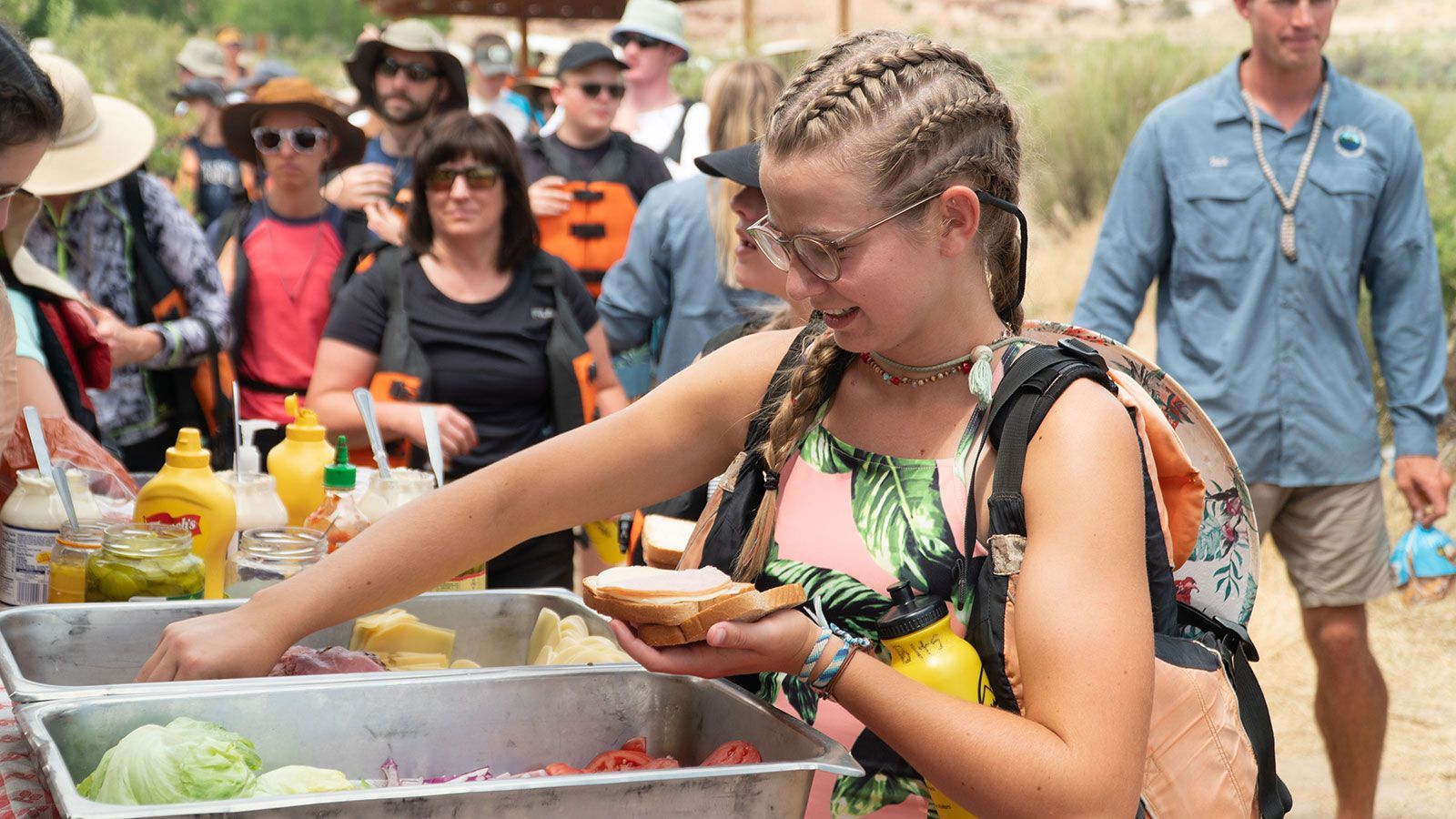 A woman is holding a sandwich in her hand in front of a crowd of people.
