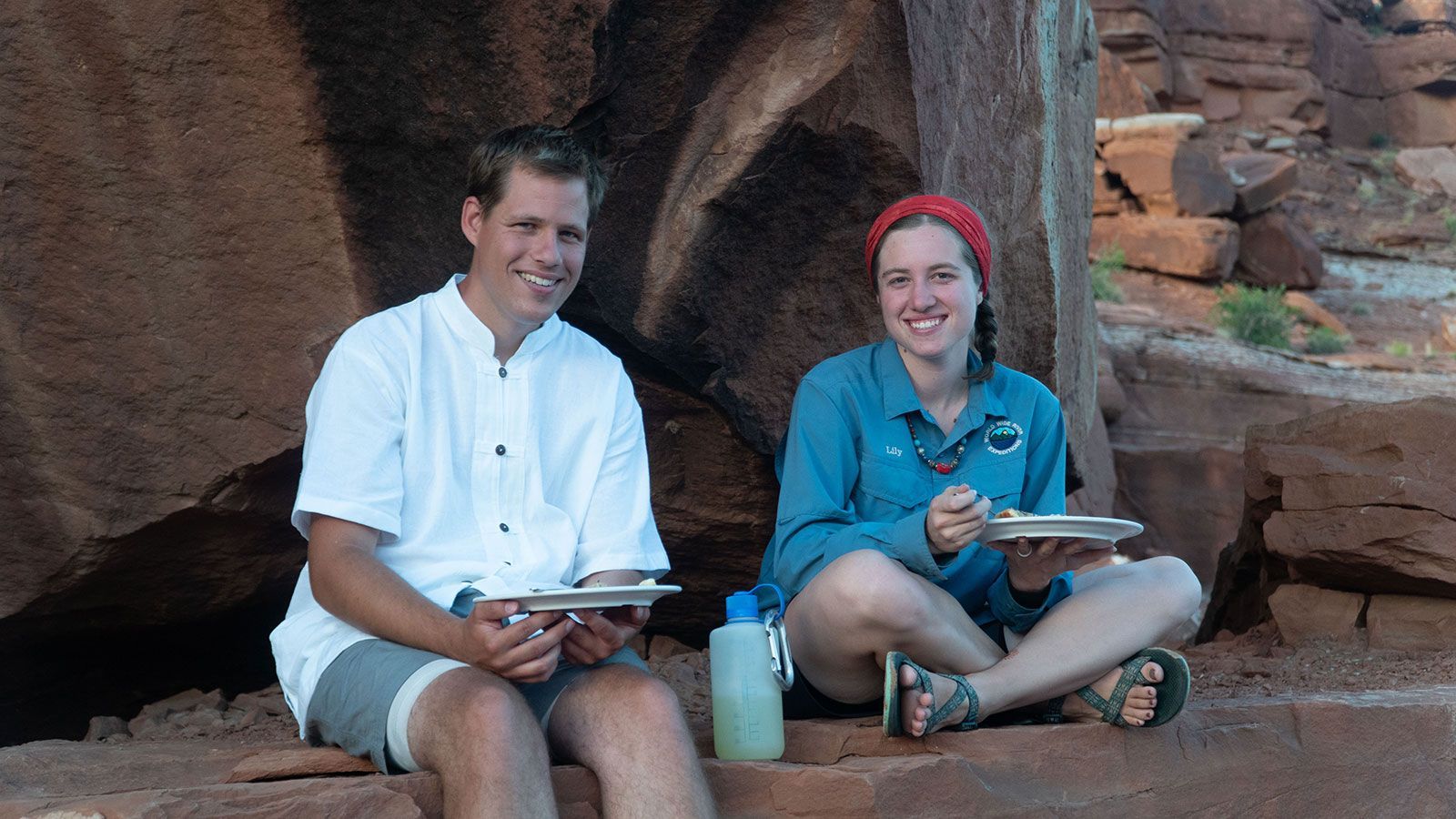 A man and a woman are sitting on a rock eating food.