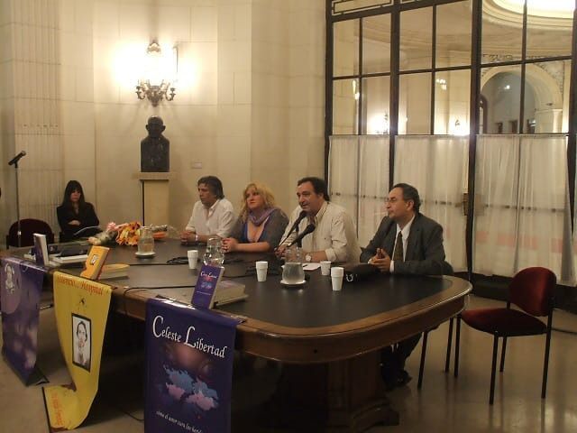 Mesa redonda en un salón formal, con pancartas y micrófonos.