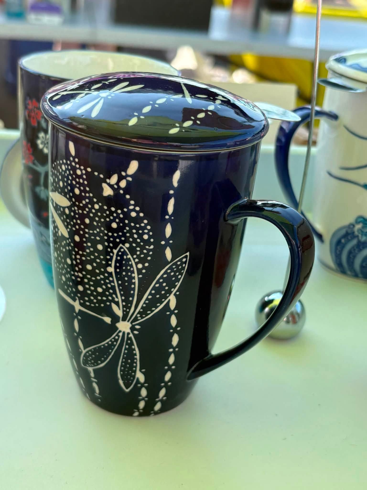 Black mug with white butterfly and floral design on a table, with a spoon in the background