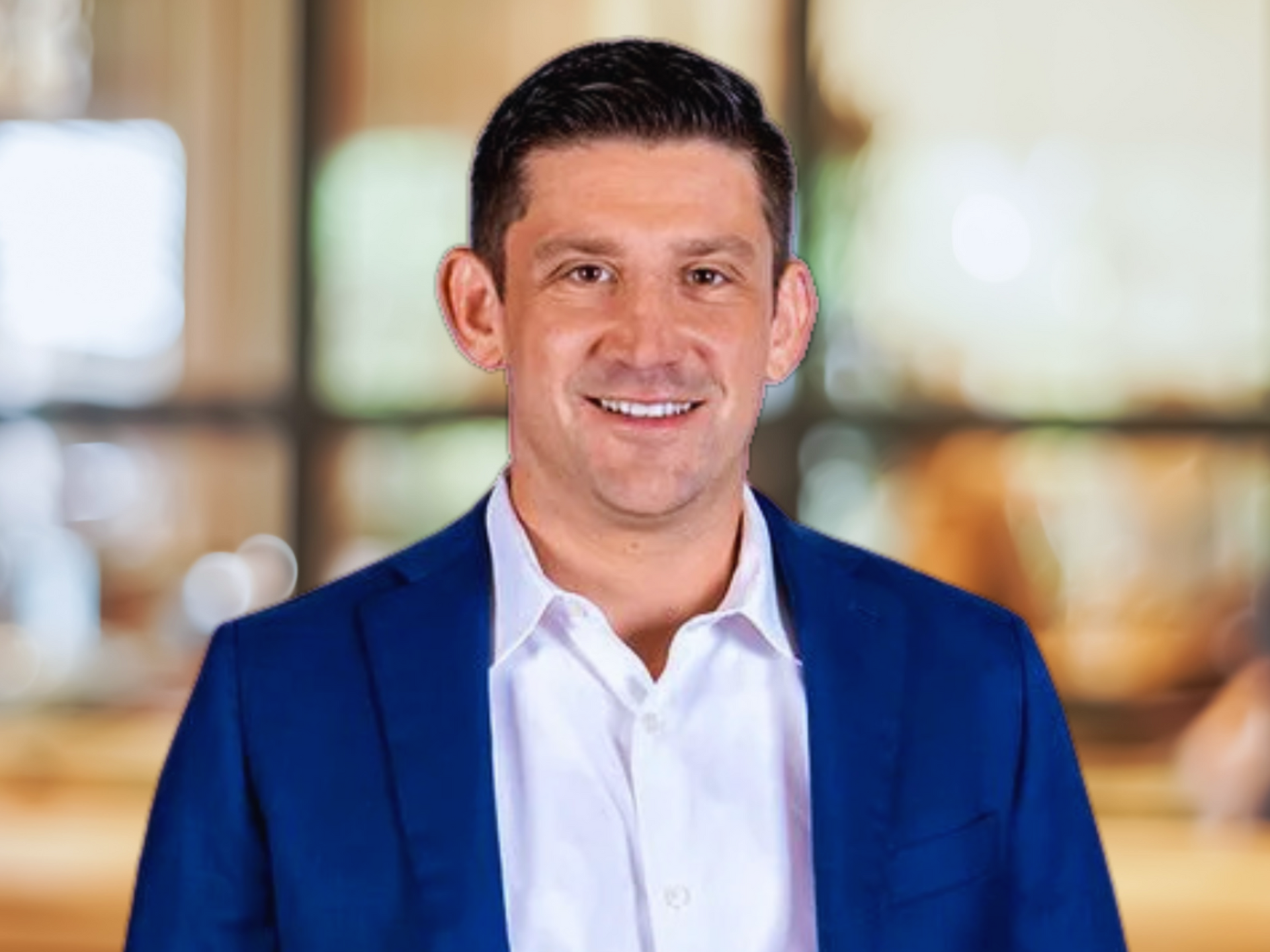 A man in a blue suit and white shirt is smiling for the camera.