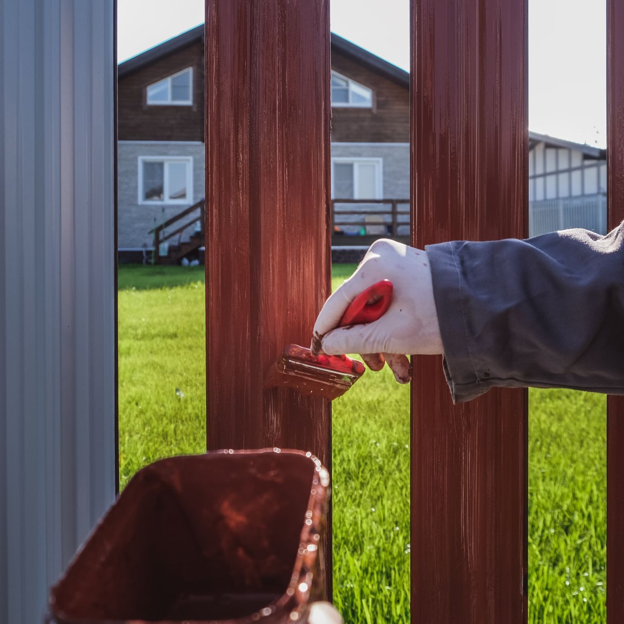 A person is painting a wooden fence with a brush.