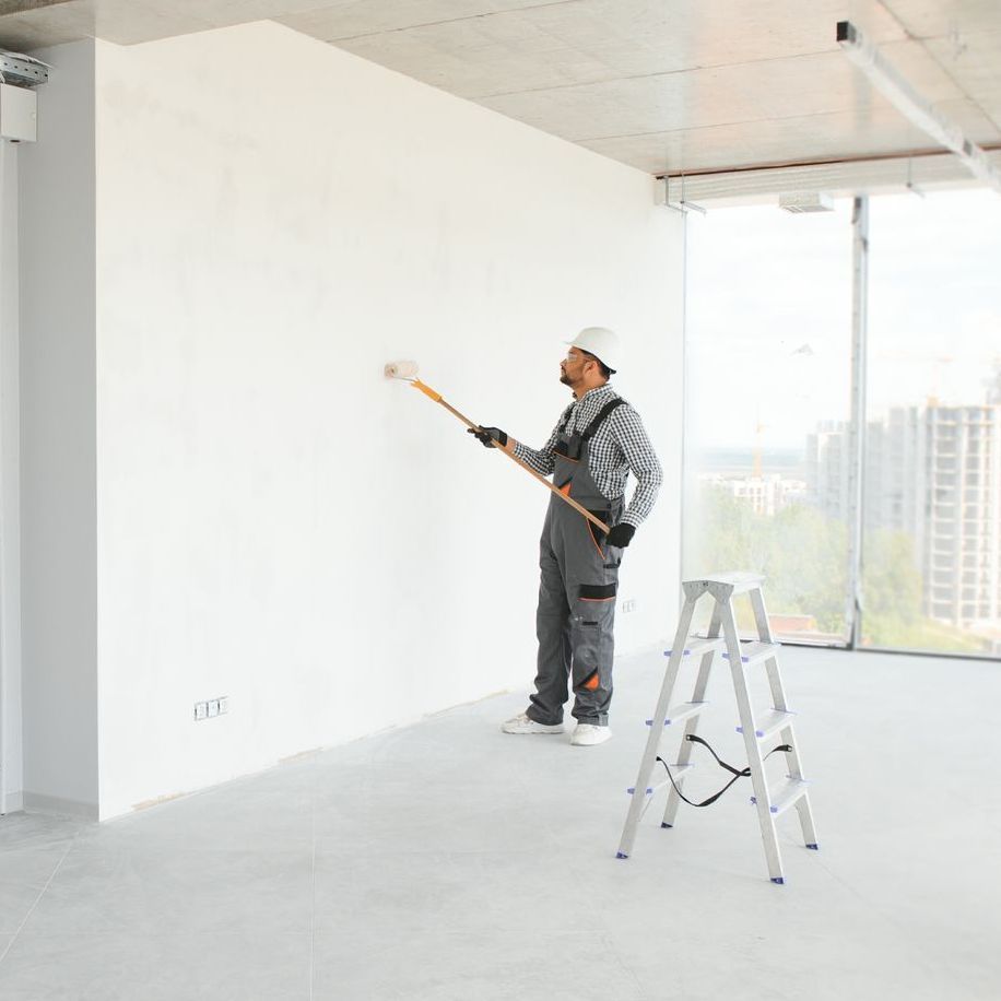 A man is painting a wall with a roller in an empty room.