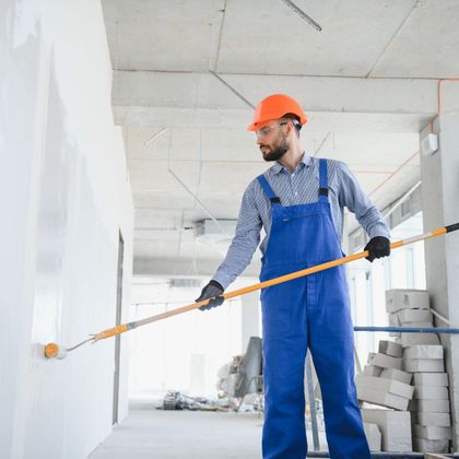 A man in blue overalls is painting a wall with a roller