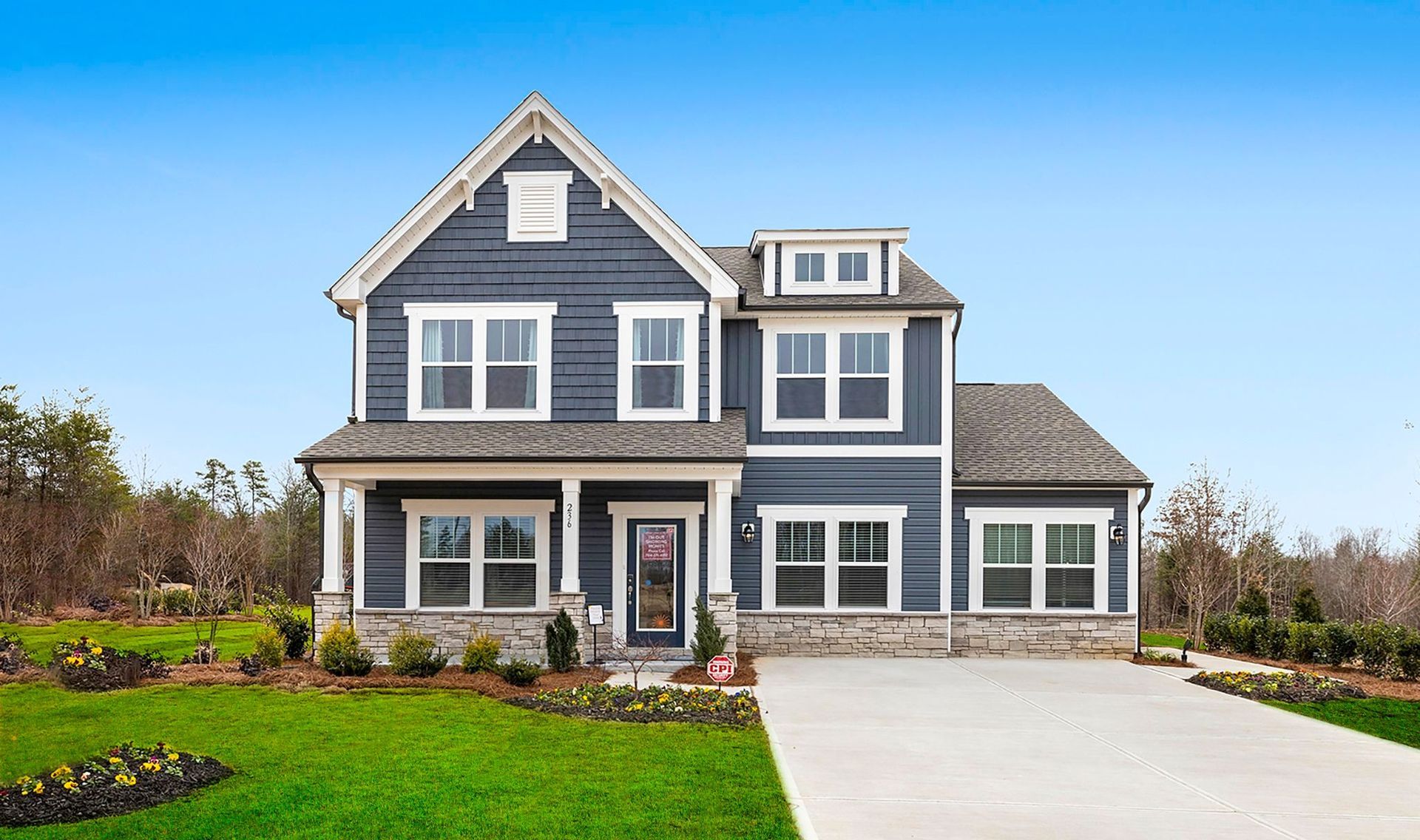 Two-story blue house with white trim and a front porch on a green lawn under a blue sky.
