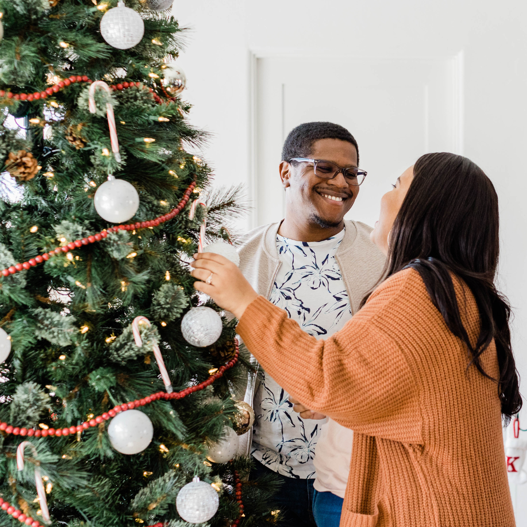 A man and a woman are decorating a christmas tree together.