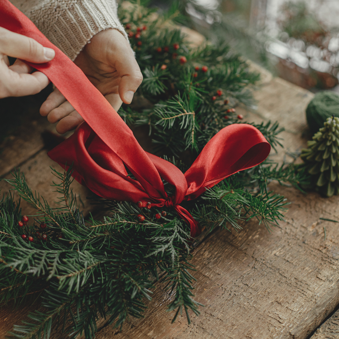 A person is tying a red ribbon around a christmas wreath.