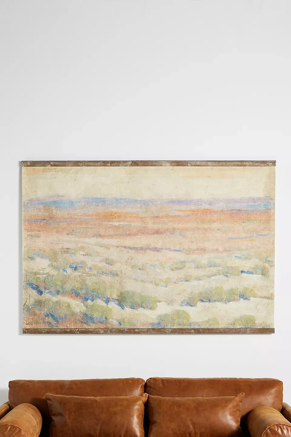 A large painting is hanging on a wall above a brown leather couch.