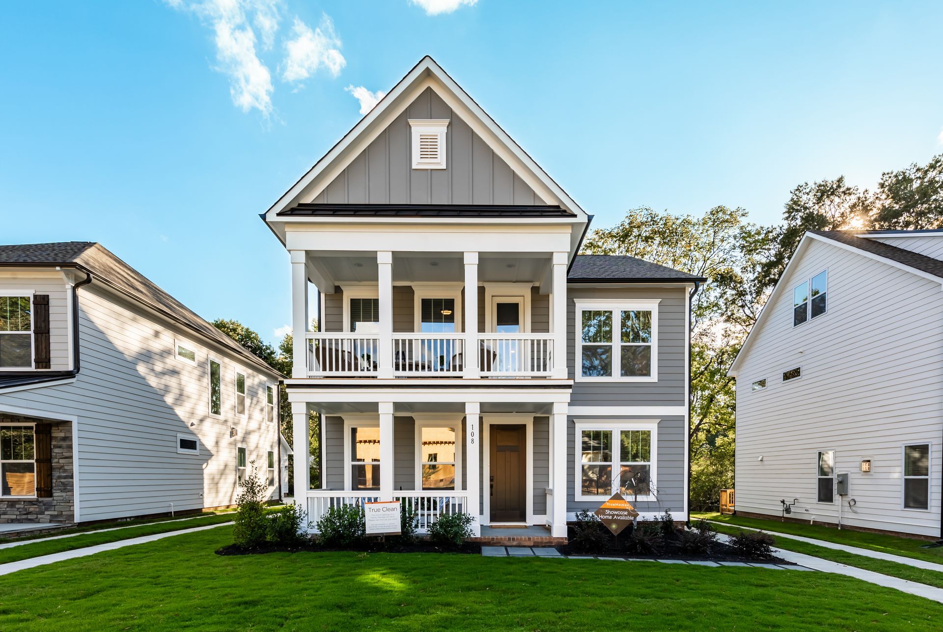 A large gray and white house with a large porch is sitting on top of a lush green lawn.