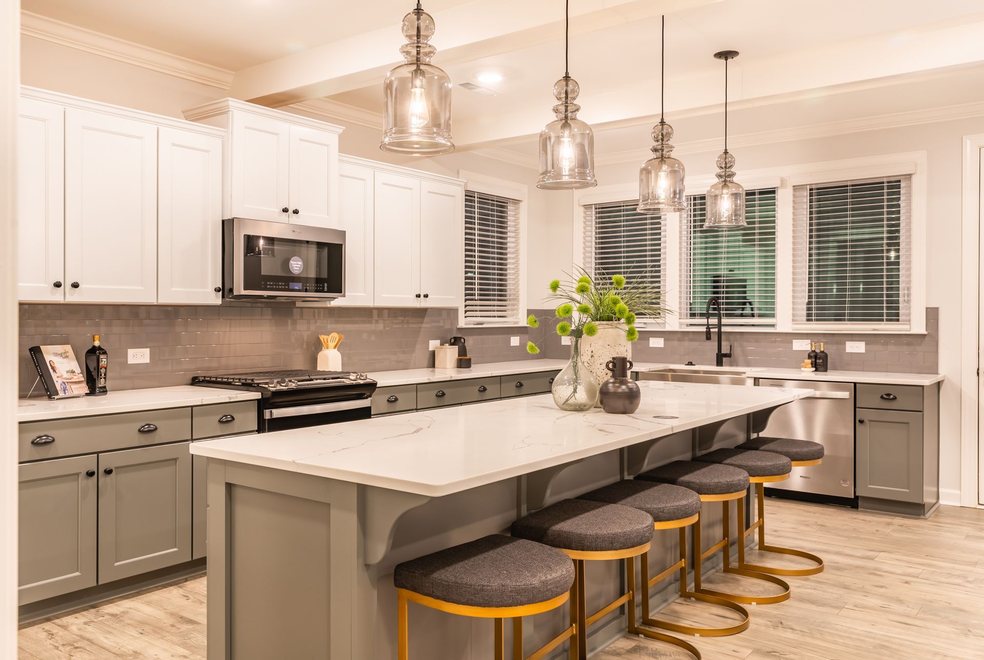 A kitchen with gray cabinets , white cabinets , stainless steel appliances , a large island and stools.