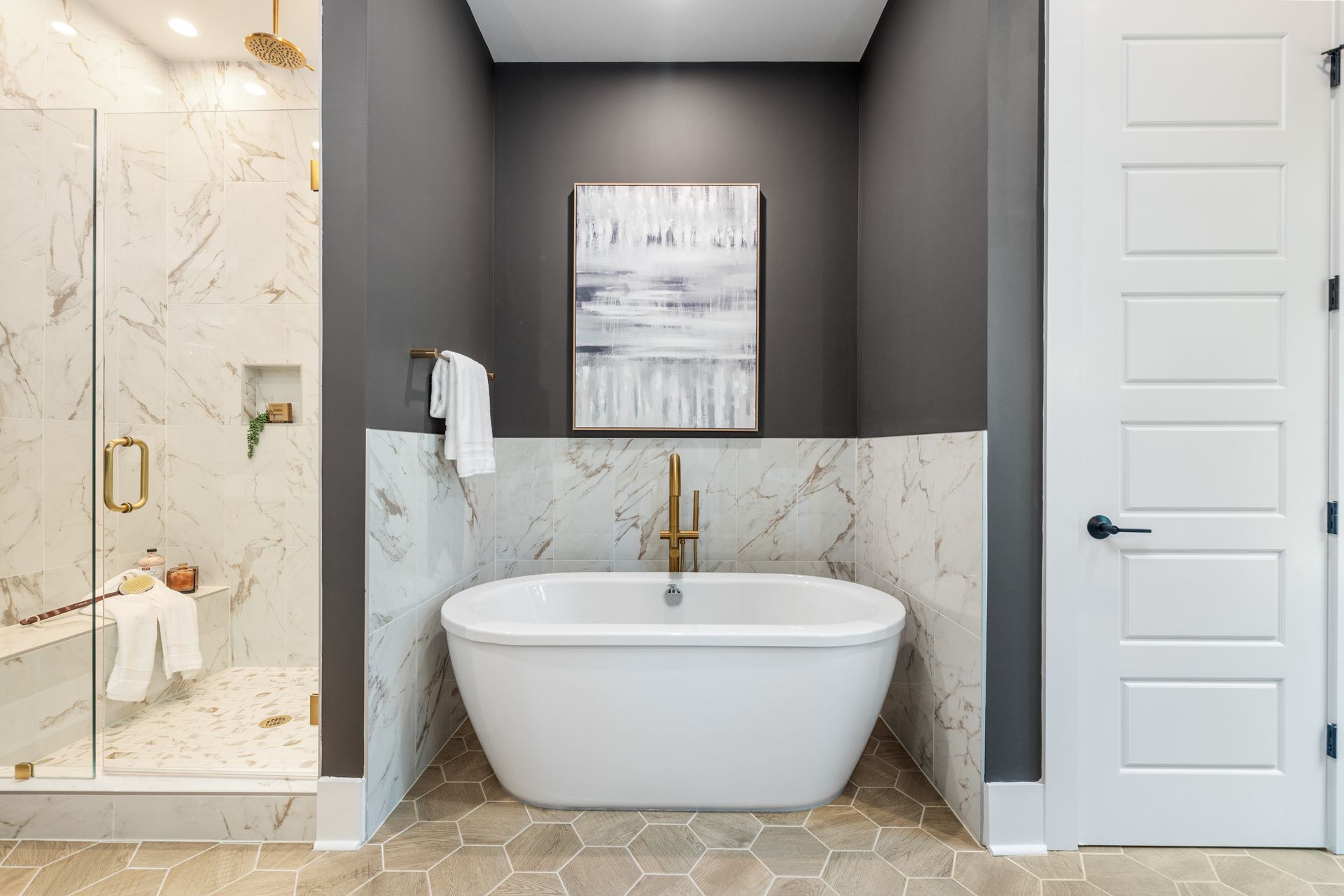Bathroom with white soaking tub, marble walls, and gray accents.