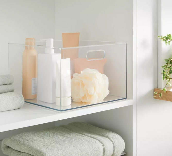A bathroom shelf with a clear container filled with soaps and towels