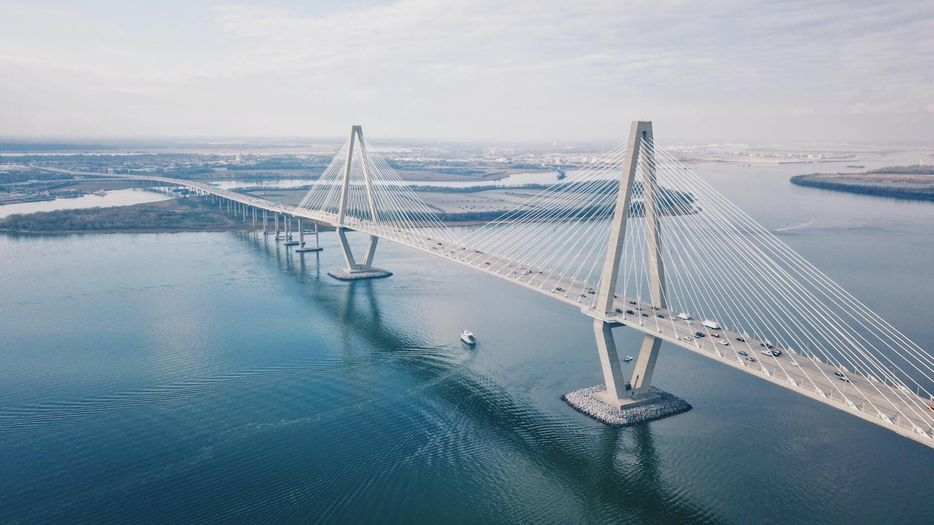 Cable-stayed bridge over blue water with a boat, in a coastal landscape.