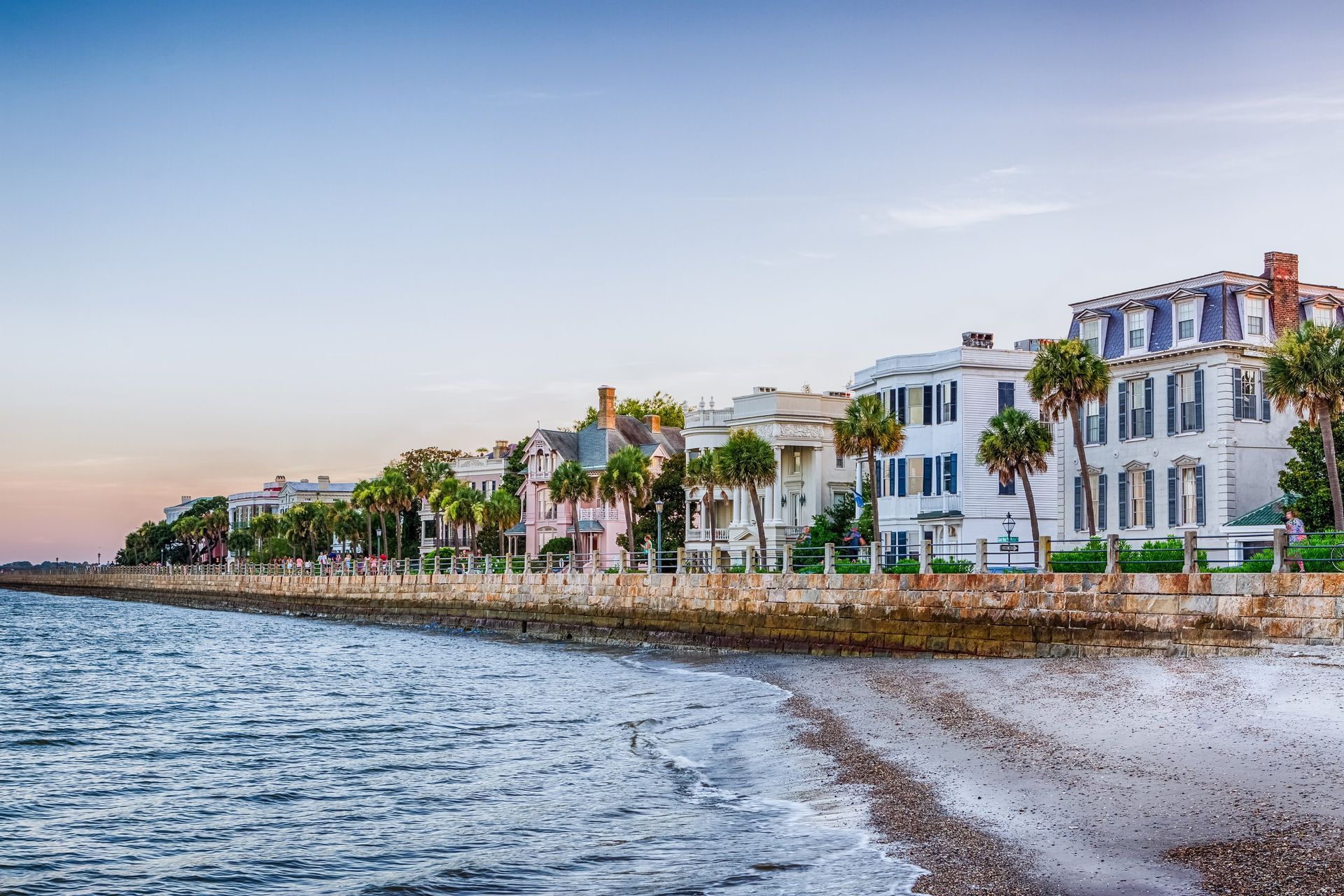 Waterfront view of Charleston, SC, showcasing historic white buildings, palm trees, and ocean.
