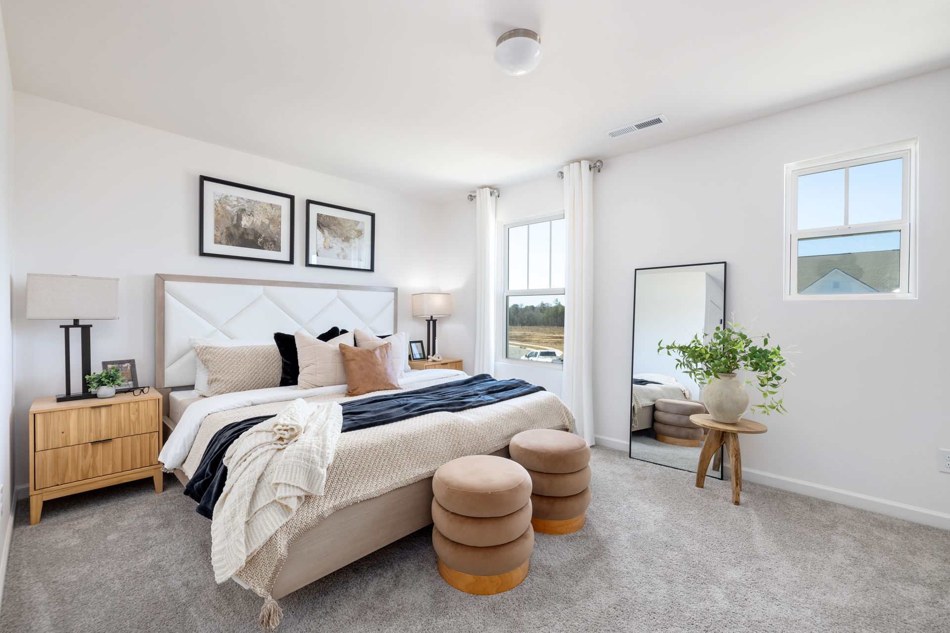 A bedroom with a large bed , two ottomans , a mirror and a window.