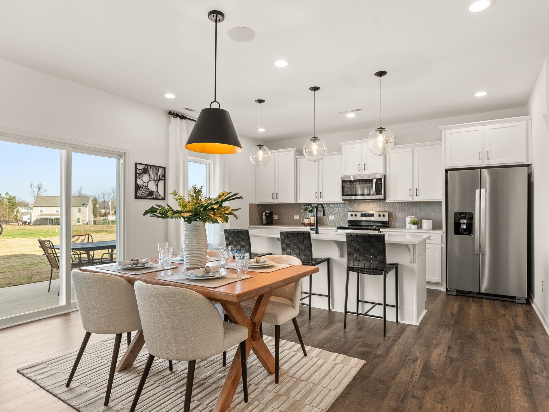 A dining room with a table and chairs and a kitchen with stainless steel appliances.