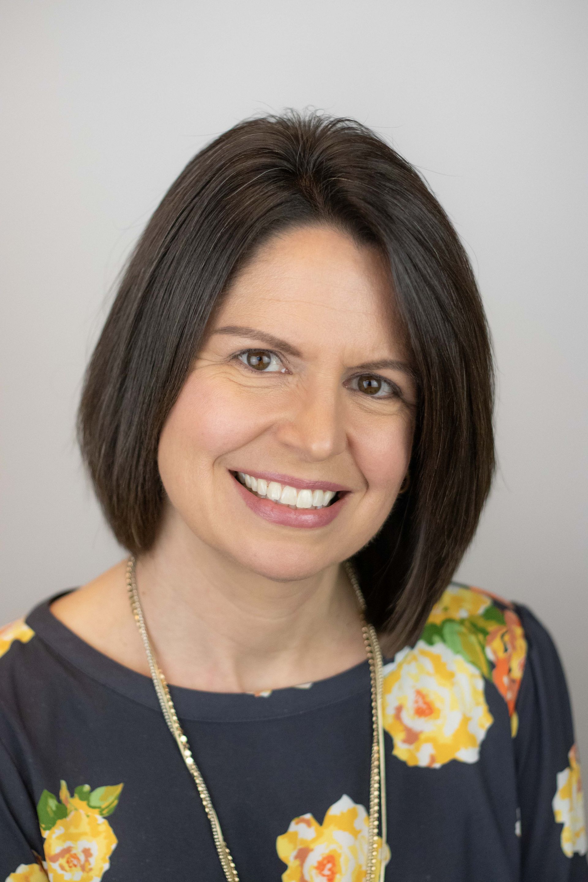 A woman wearing a floral shirt and necklace is smiling for the camera.