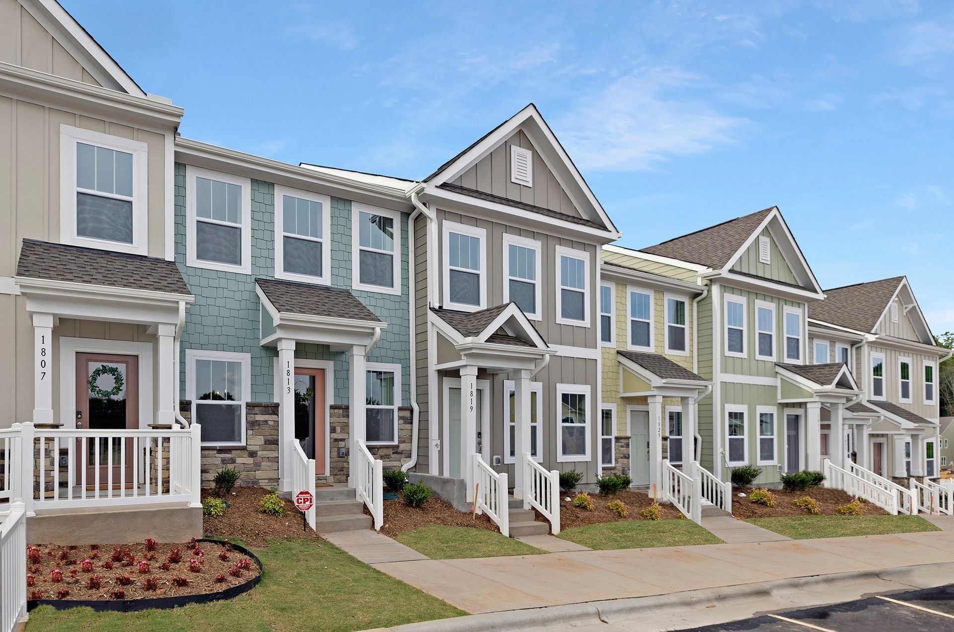 Row of townhouses in various colors, with cars parked in front.