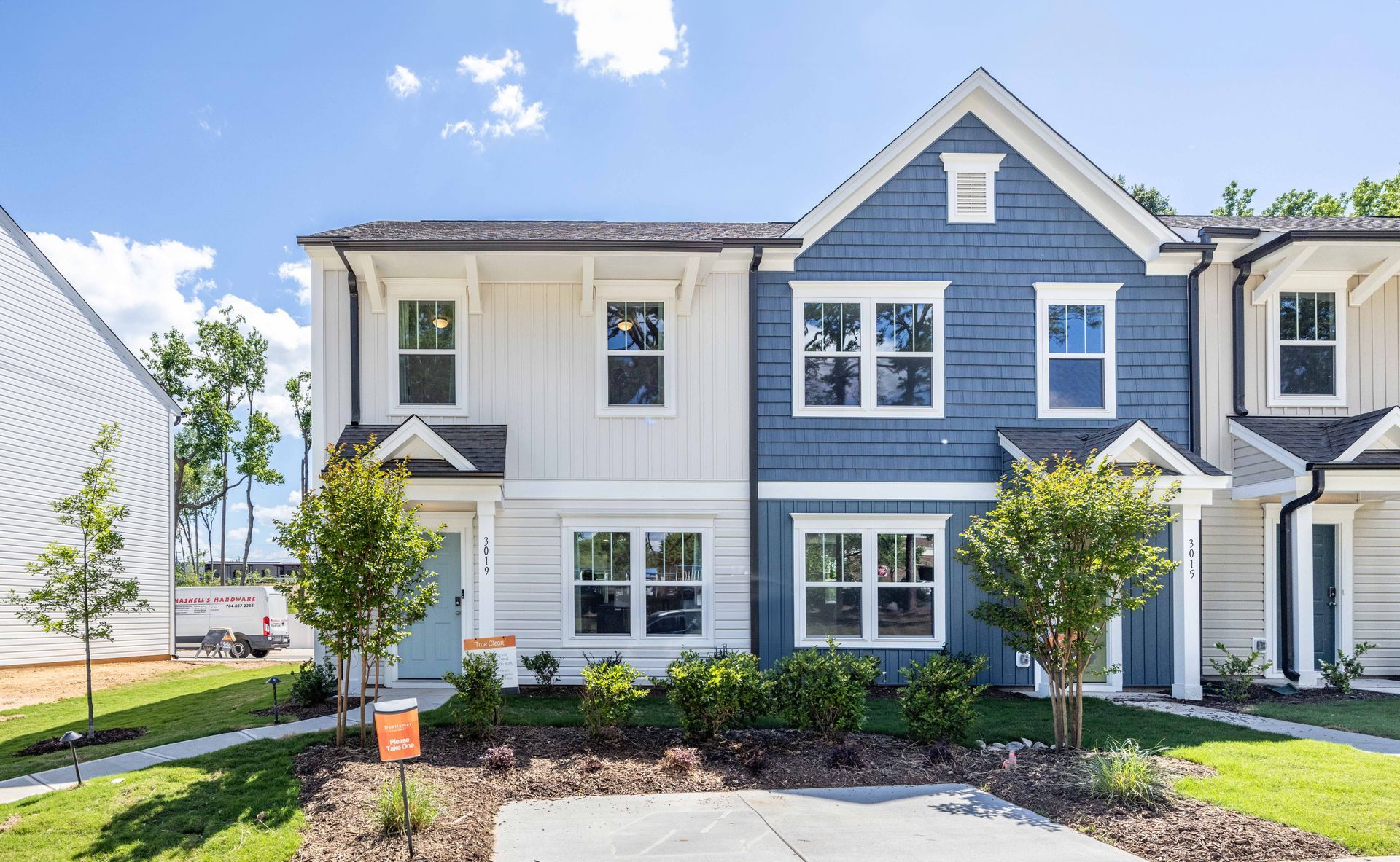Row of modern blue-and-white townhouses with front lawns and young trees under a bright sky