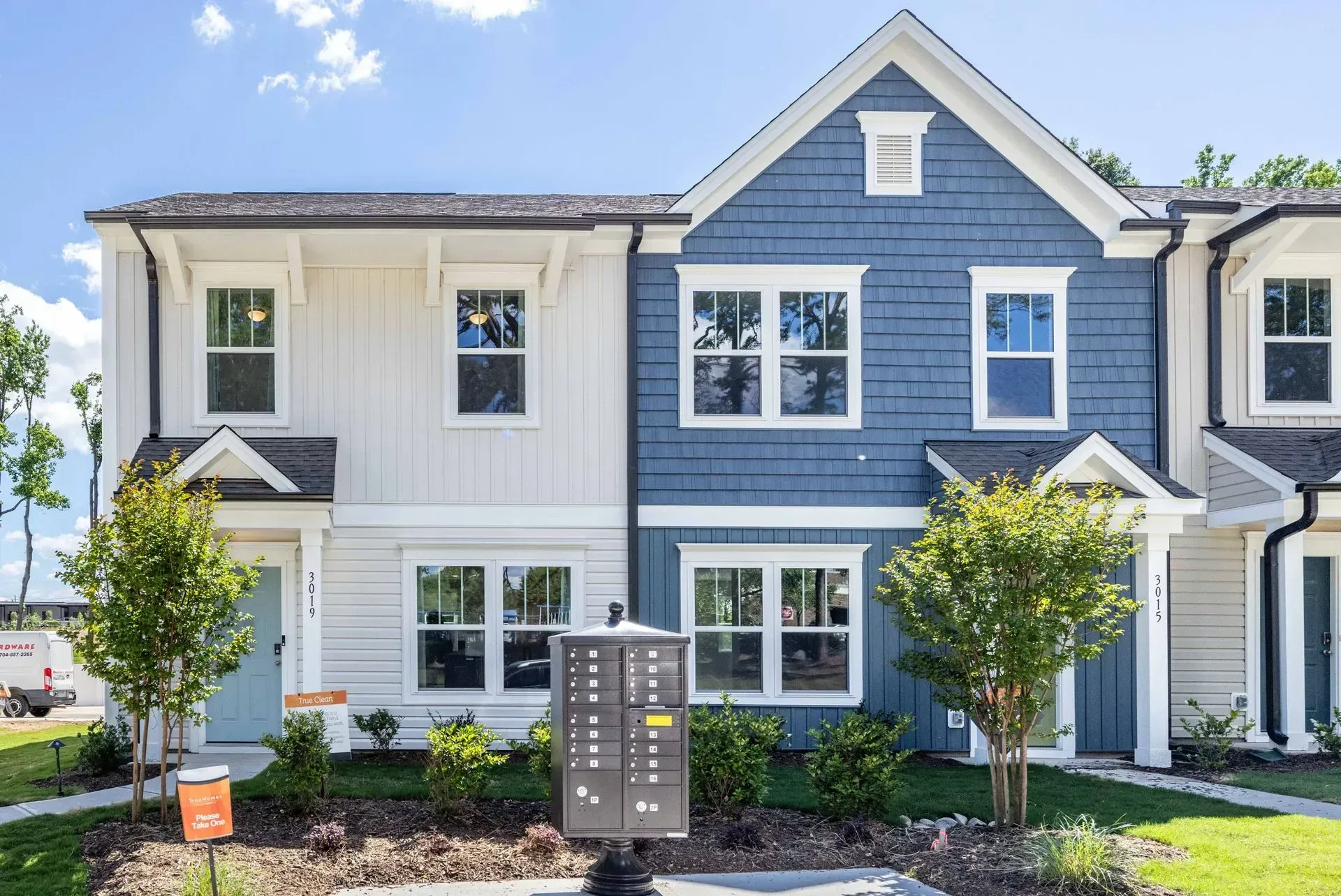 Row of modern townhouses with blue and white siding, front doors, windows, and small landscaped yards