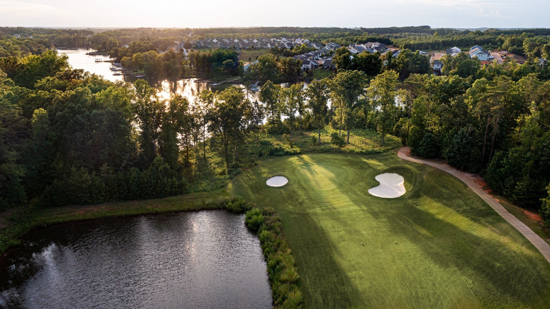 Golf course hole next to water, with sand traps and trees.