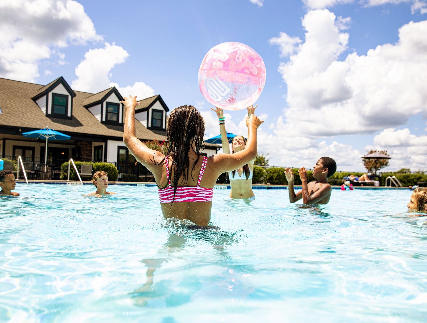 A girl is holding a pink ball in a swimming pool.