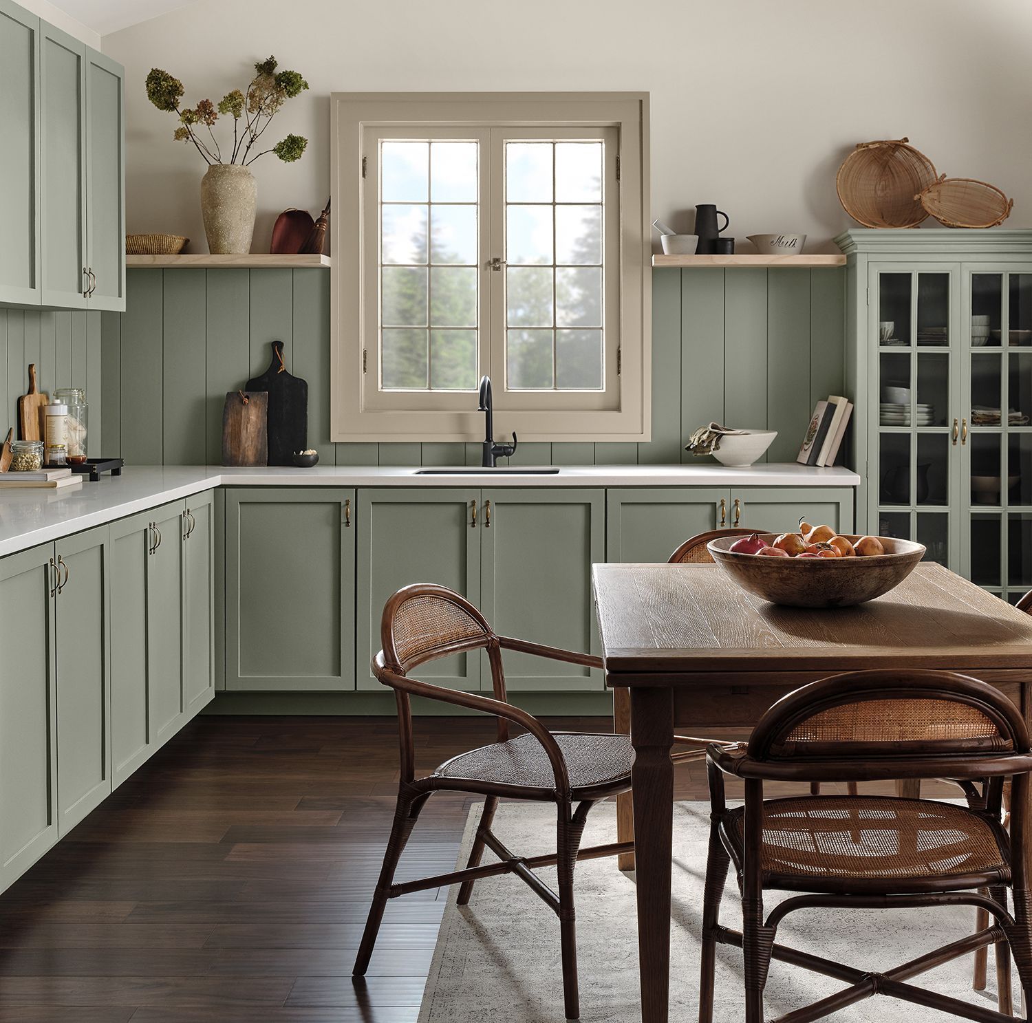 A kitchen with green cabinets and a table with a bowl of fruit on it