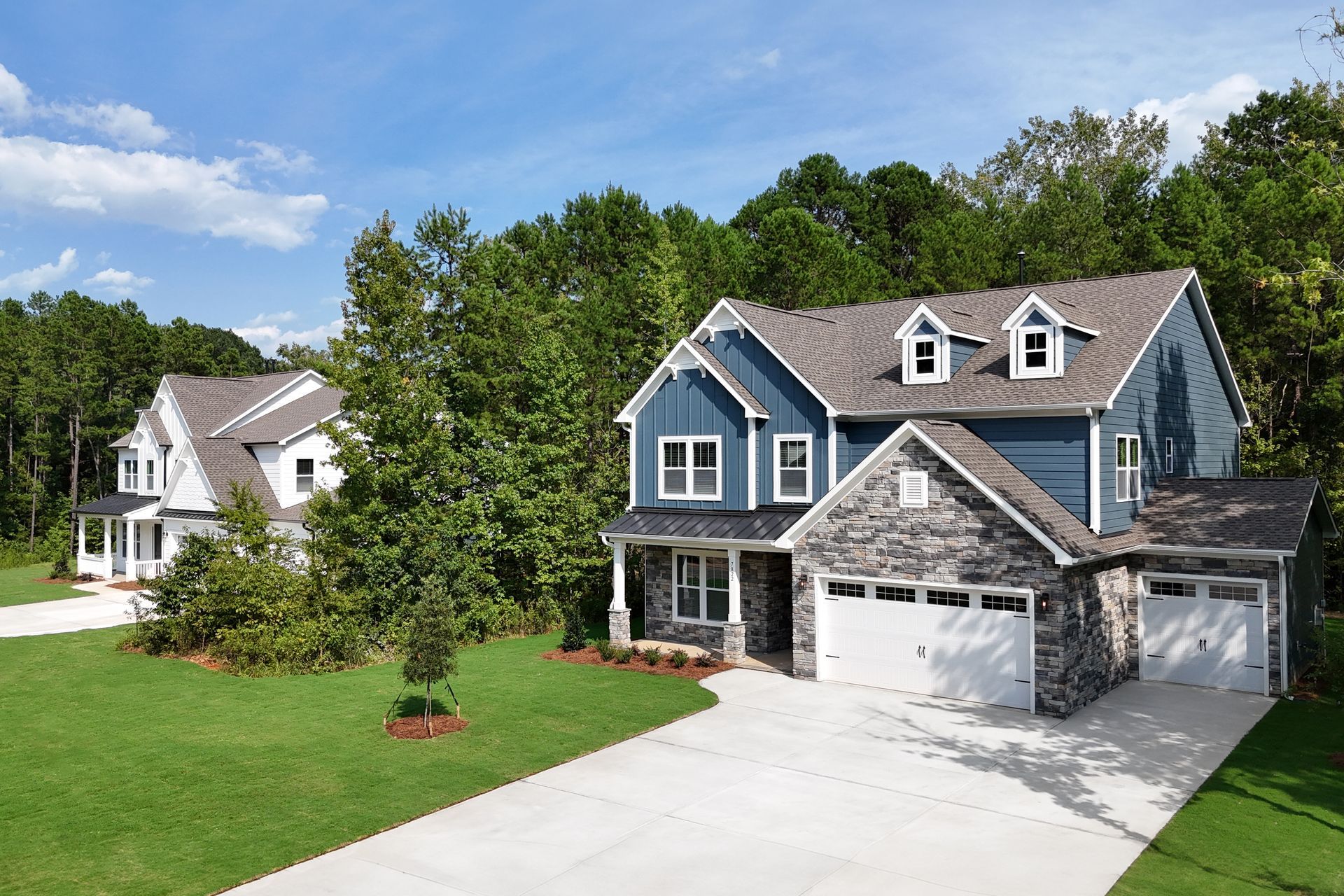 Two-story homes with blue and white siding, stone accents, and attached garages in a wooded area.